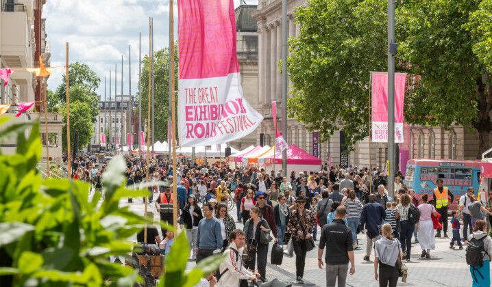 A photograph of a crowd of people at the Festival, with pink flags in the forefround.